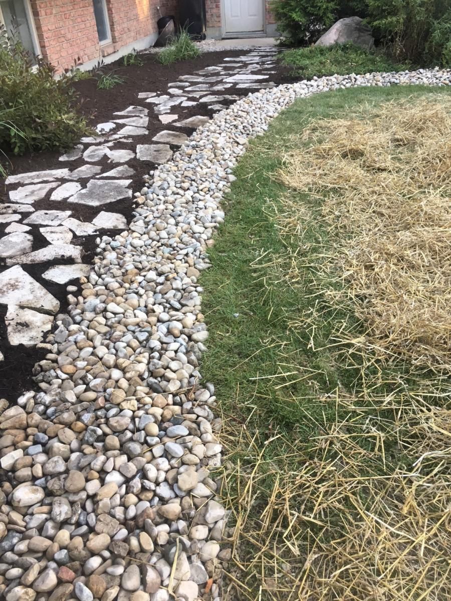 Stone walkway beside a gravel border and grassy yard near a brick house entrance