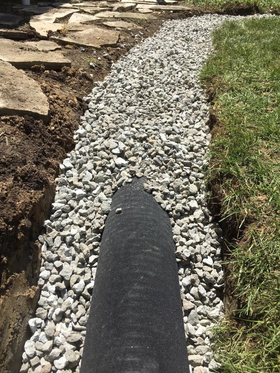 A gravel path beside rocks and grass, with a black edging strip in the foreground.