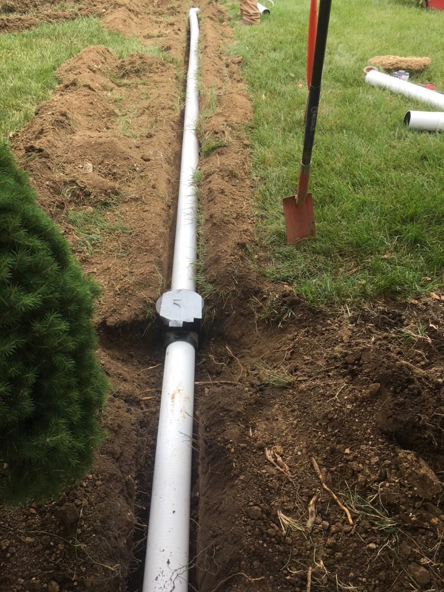 Trenched white PVC pipe with a valve in a grassy yard beside a shovel