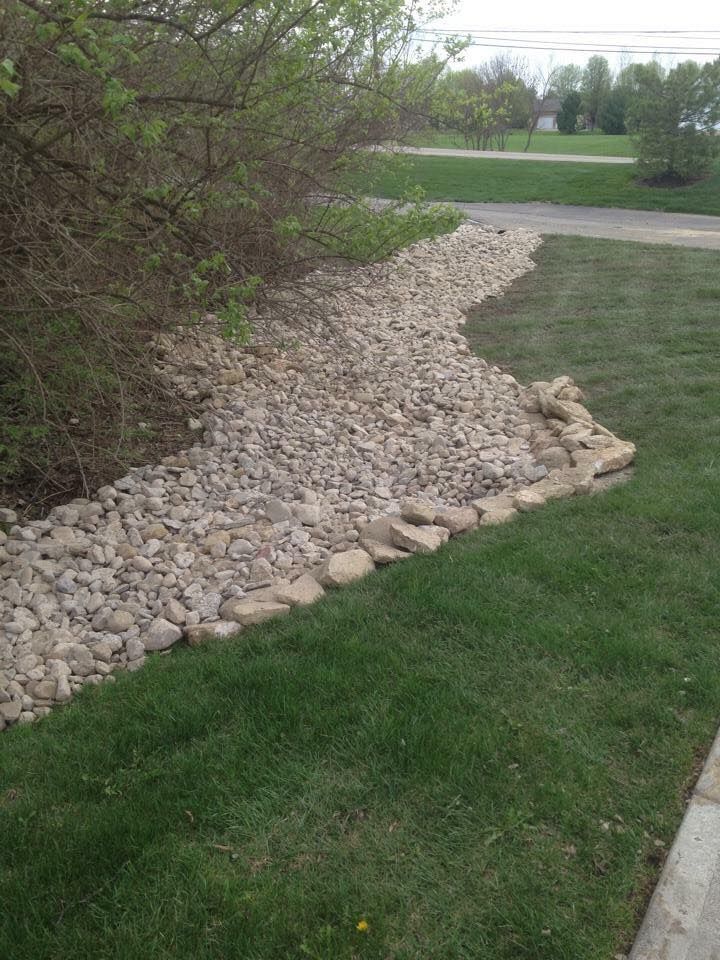 Rock-lined drainage swale beside a grassy lawn and roadside curb