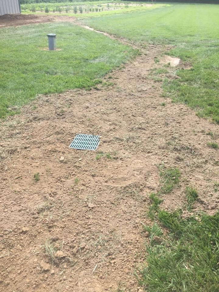 Dirt path through a grassy field with a blue utility cover and a small vent post nearby.