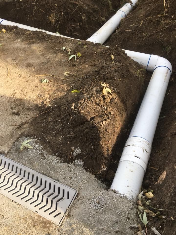 Damaged white drainage pipe beside a dirt trench and storm drain grate