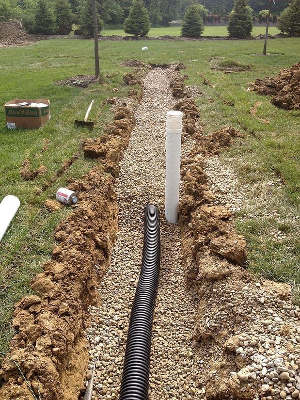 Trenched ground with a black drainage pipe and white vertical pipe in a grassy field