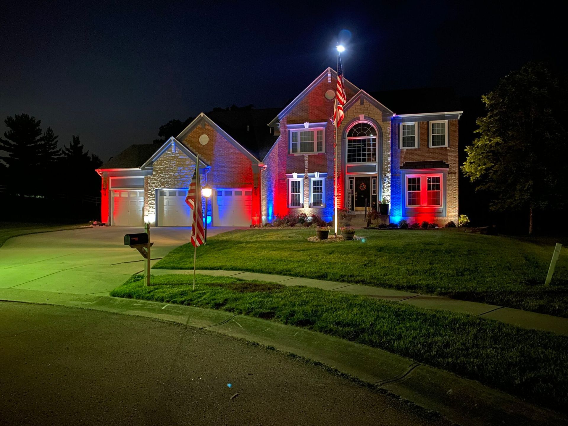 House lit with red and blue lights at night, with a bright front lawn and driveway