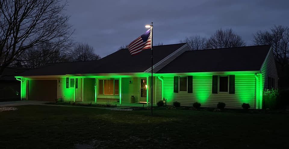 House lit with green lights at dusk, with an American flag on a flagpole in front