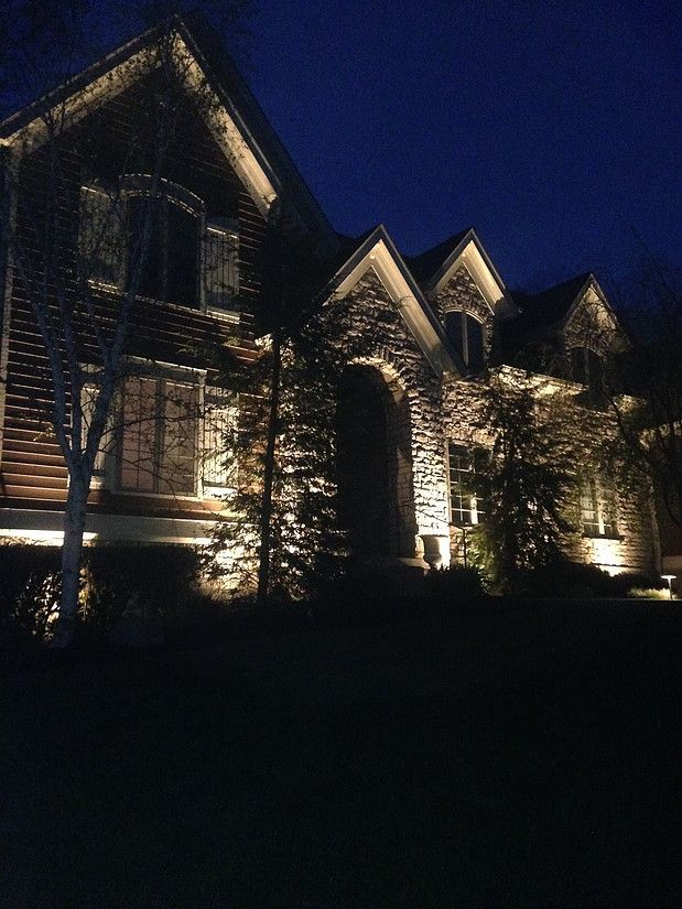Lit stone house exterior at night with gabled roofs and ivy-covered walls