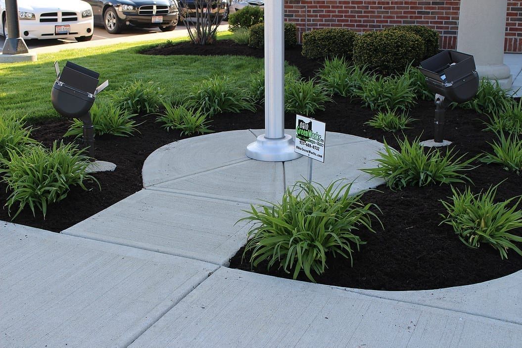 Concrete walkway through landscaped planting beds around a pole base under a covered area