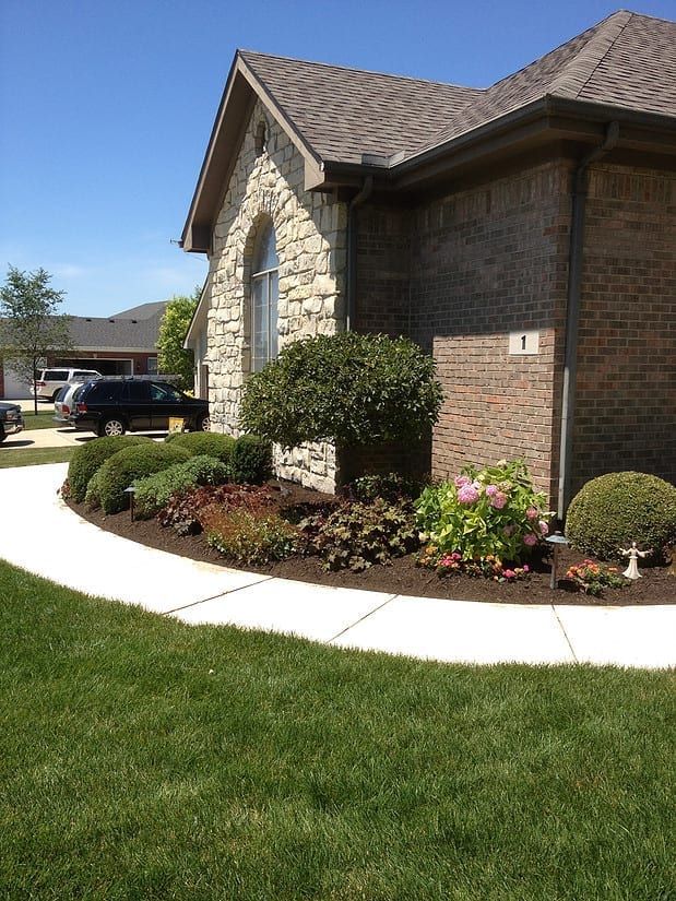Brick house exterior with curved walkway, green lawn, and landscaped shrubs under a clear blue sky