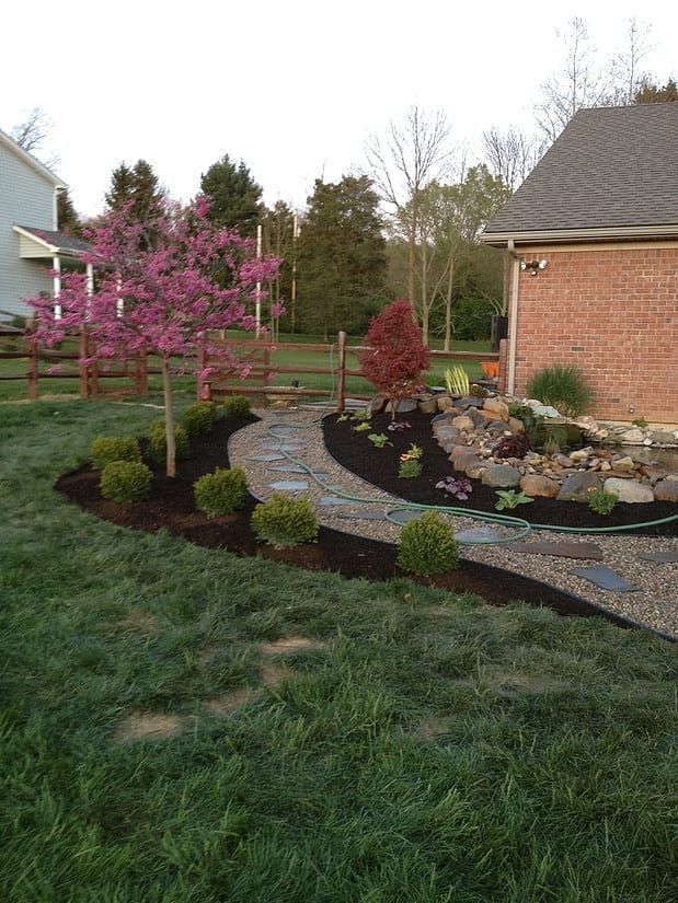 Landscaped front yard with pink flowering tree, shrubs, stone border, and a brick house