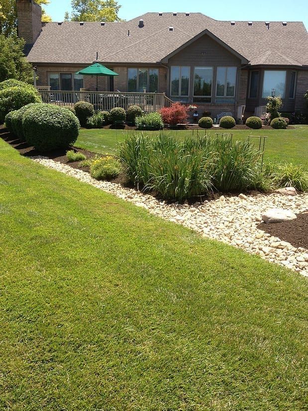 Backyard with manicured lawn, stone planter bed, and a patio-covered house in the background