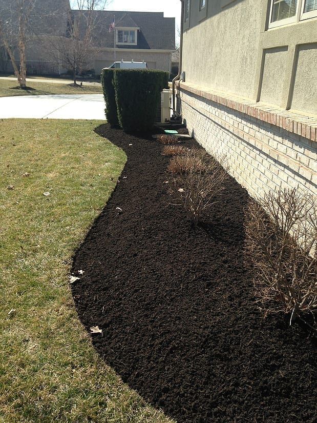 Freshly mulched landscaping bed along a house beside a green lawn and trimmed shrub.