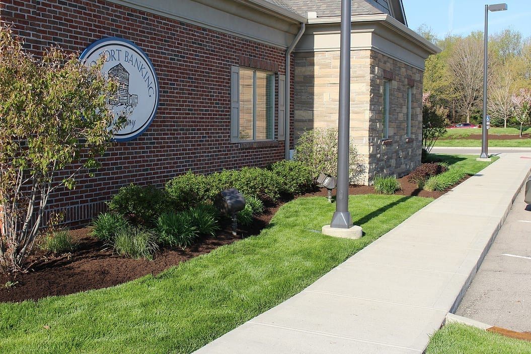 Brick building with landscaped flower beds, a sidewalk, and a lamppost along a street