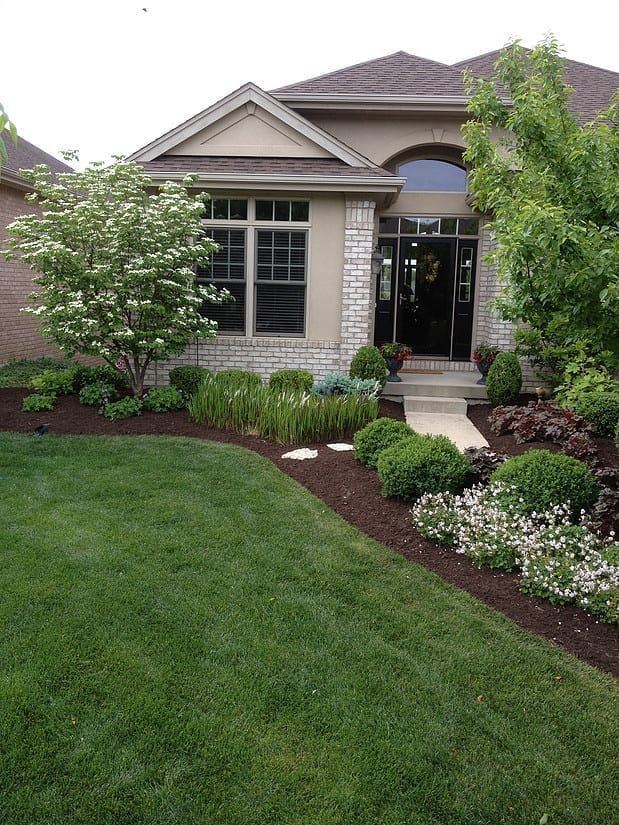 Landscaped front yard with a stone house, green lawn, and flowering shrubs leading to the entrance
