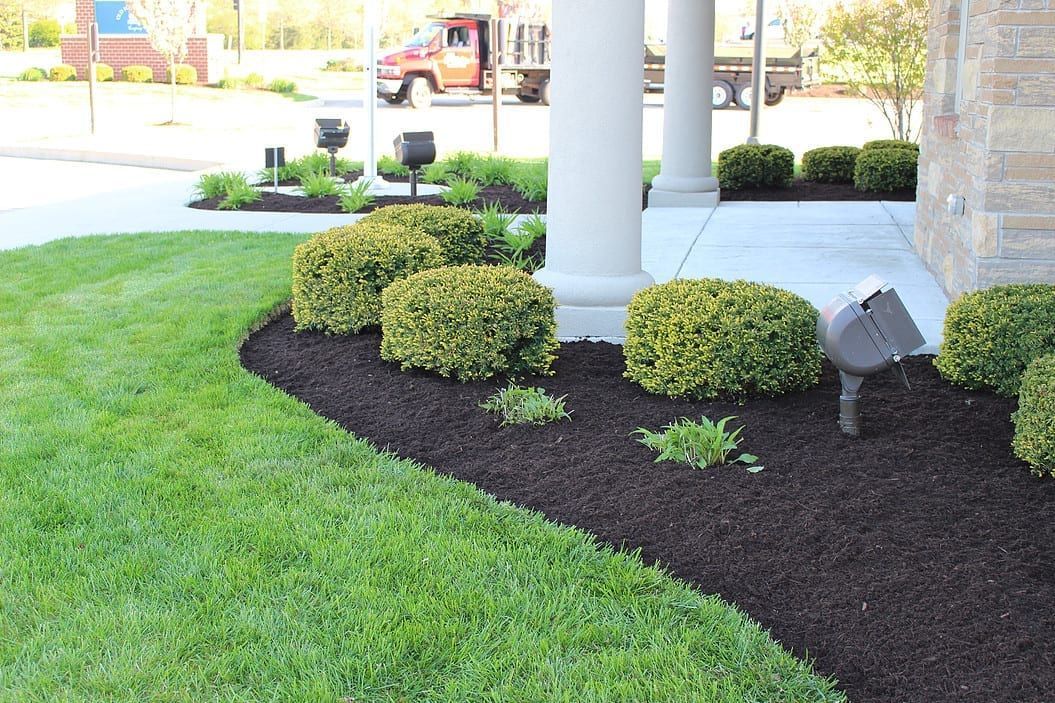 Landscaped building entrance with green lawn, dark mulch beds, shrubs, and white columns