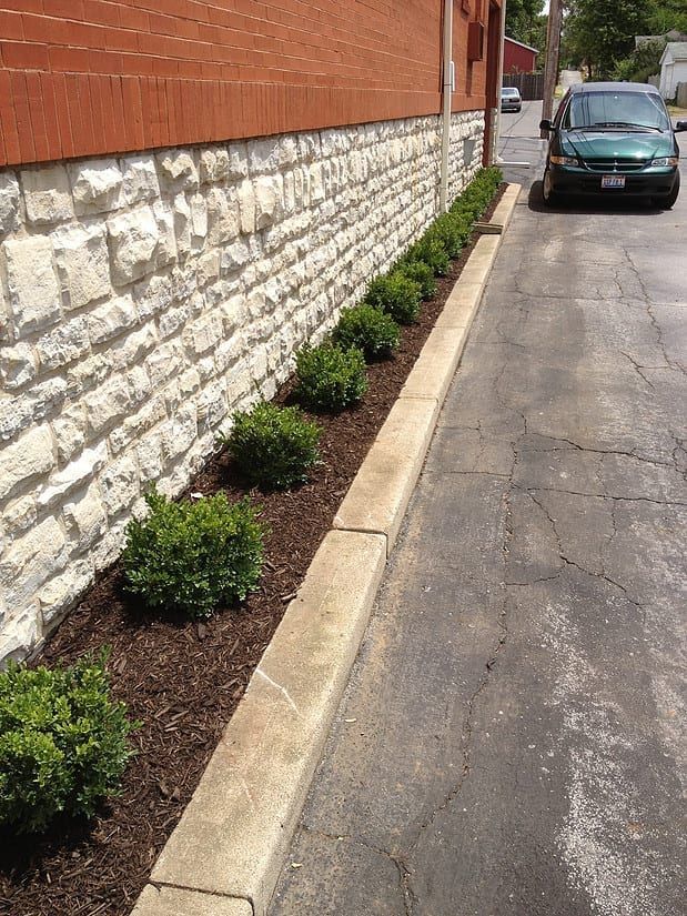 Narrow alley beside a stone wall with small shrubs and a parked green car at the end.