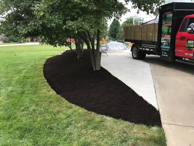 Mulched tree bed beside a sidewalk and grass, with a truck parked on the right.