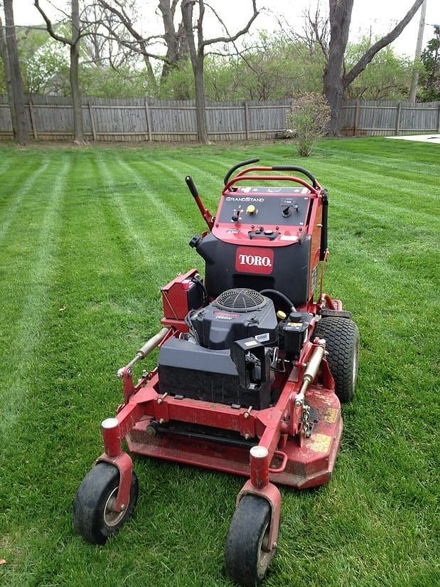 Red riding lawn mower on a striped green lawn near a wooden fence and trees