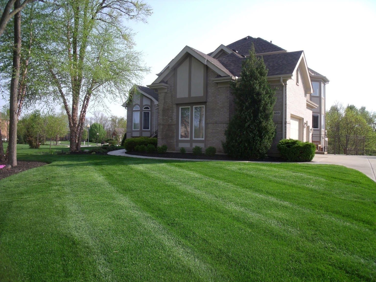 Brick house with a steep roof and manicured green lawn beside trees on a sunny day