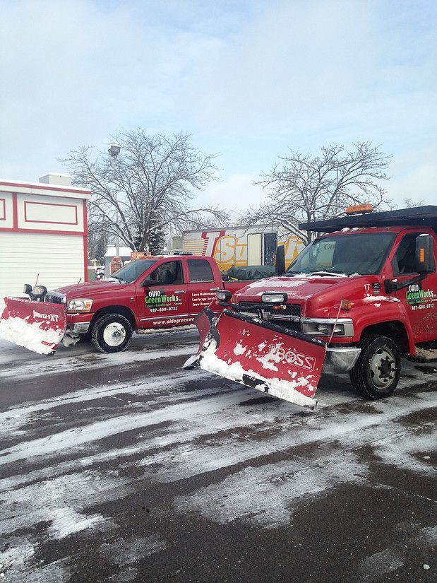 Two red snow plow trucks parked on a snowy lot with blades raised.