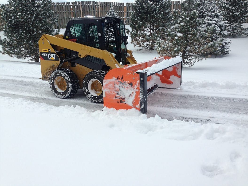 Yellow skid-steer plowing snow on a snowy driveway with an orange snow blade