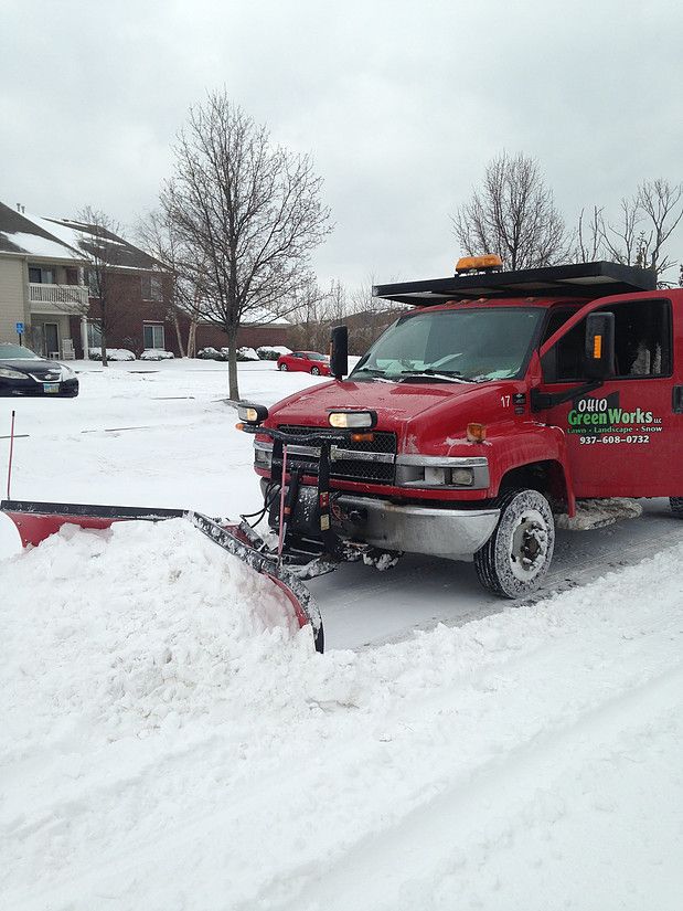 Red snowplow truck clearing a snowy residential street near houses