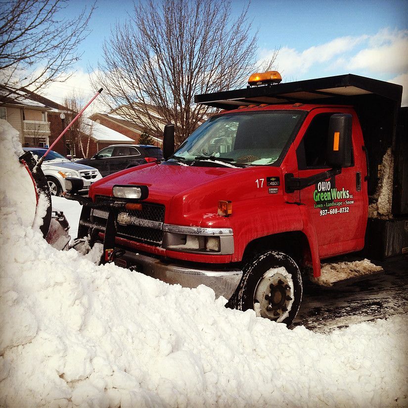 Red snowplow truck clearing deep snow in a residential driveway