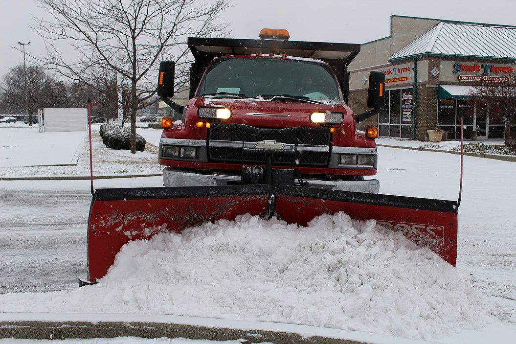 Red snowplow clearing a snowy parking lot in front of a building.