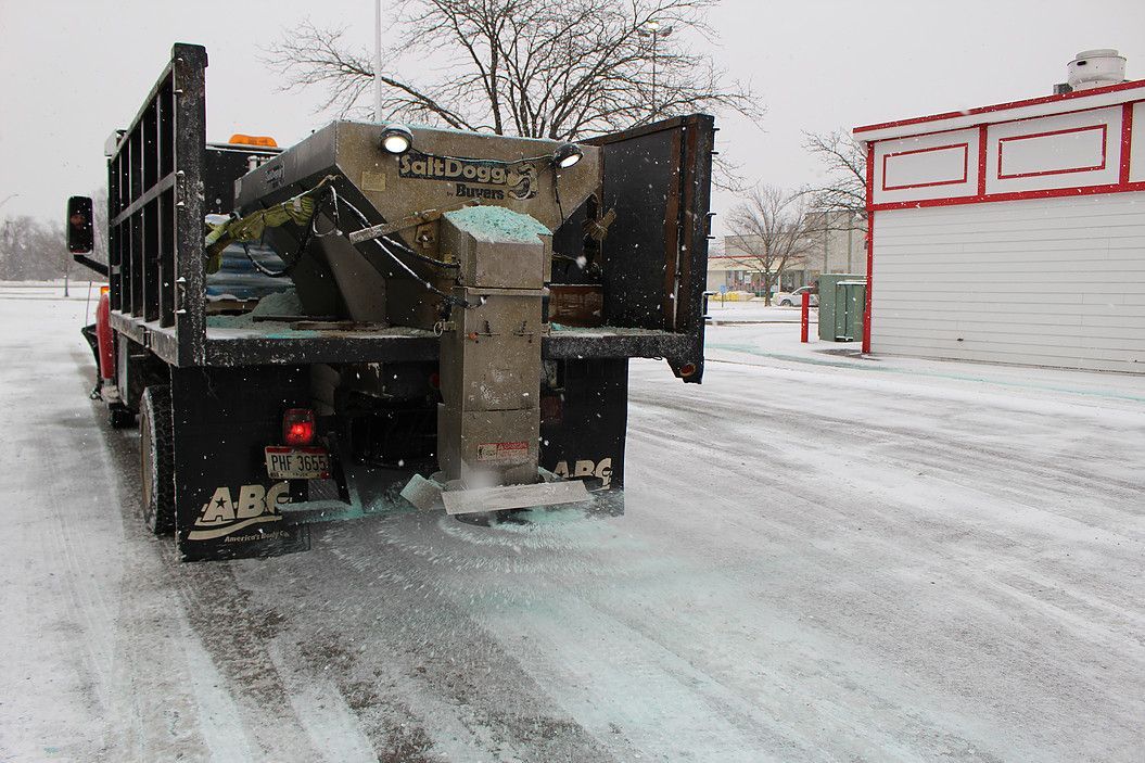 Flatbed truck hauling military equipment on a snowy road beside red-trimmed buildings