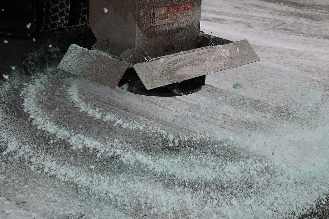 A metal machine spills white granules onto a surface, forming curved piles.