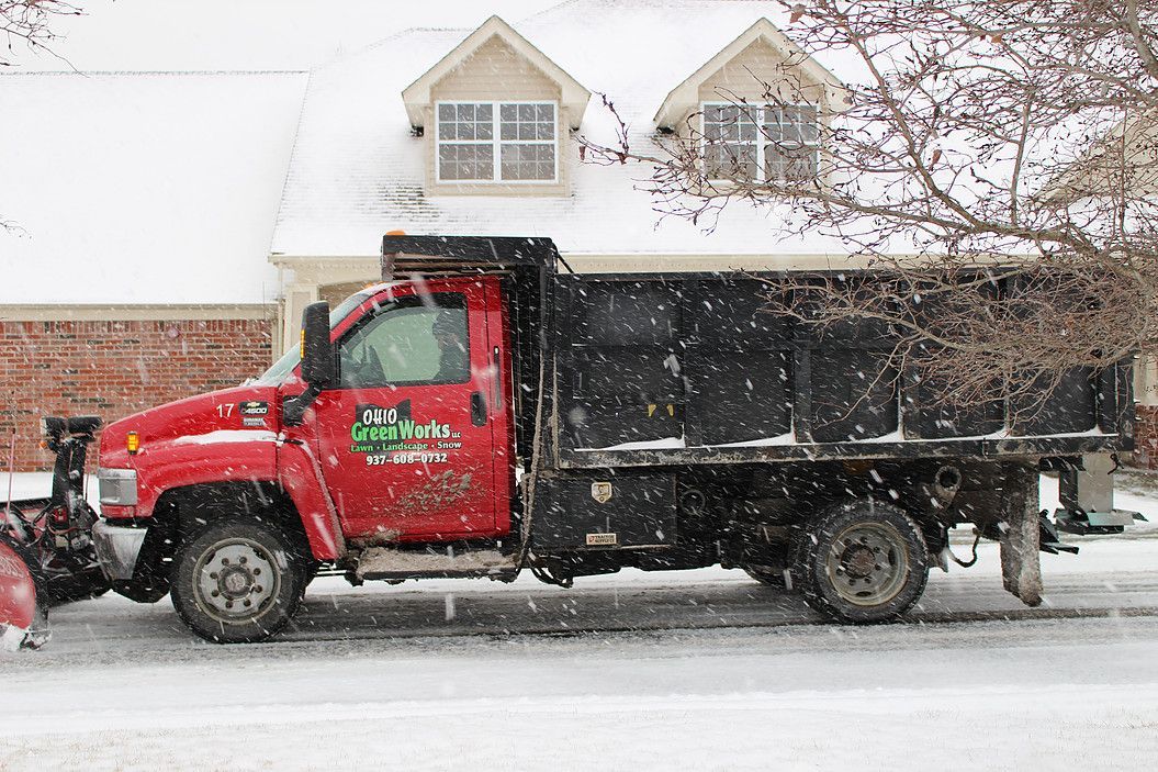 Red dump truck driving through heavy snow on a residential street.