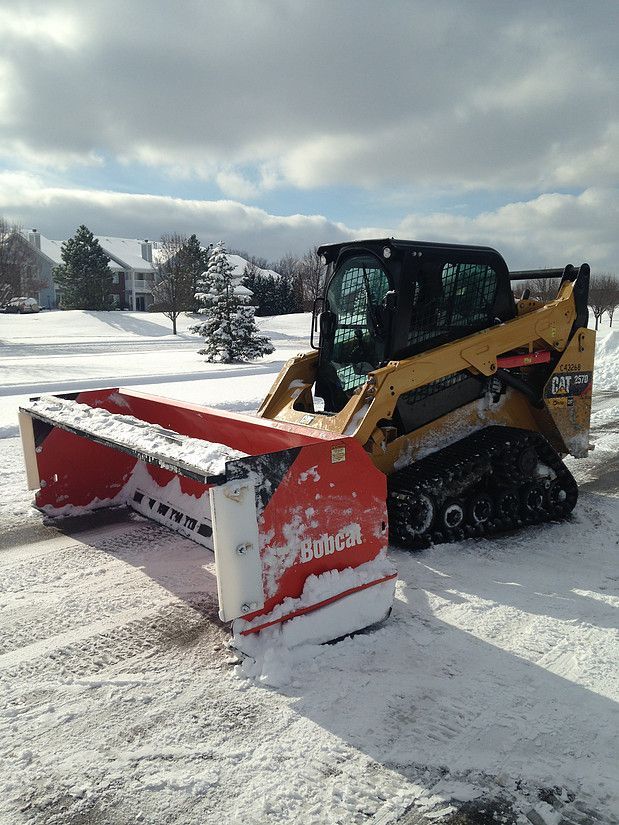 Yellow skid steer with red snowplow clearing snow on a snowy street under cloudy skies