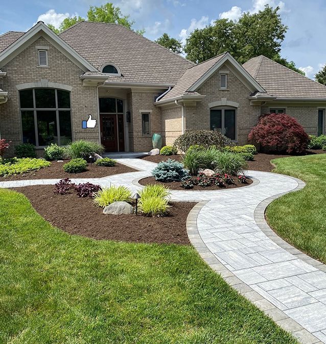 Landscaped brick house with curved paver walkway and flower beds under a bright sky