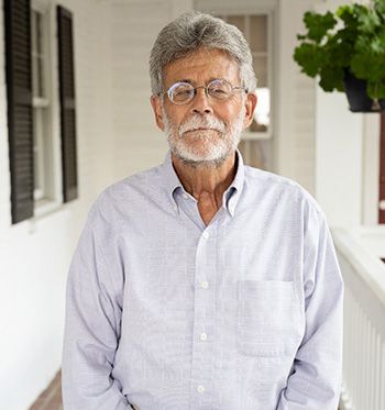 A man with a beard and glasses is standing on a porch.