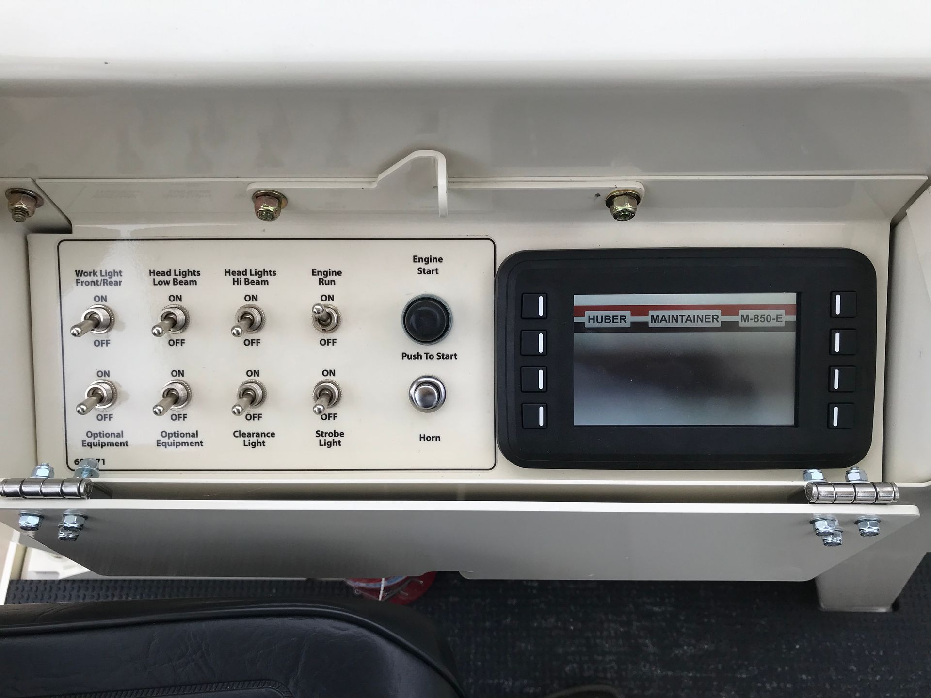 Dashboard with switches, gauges, and a digital display in a light-colored aircraft cockpit.