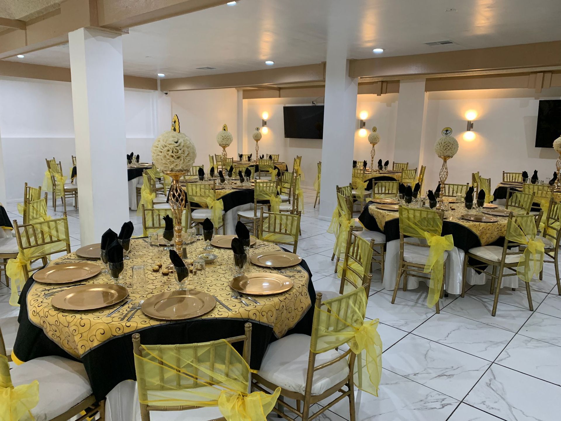 Banquet hall with round tables set for a formal event. Black and gold decor, with yellow chair accents.