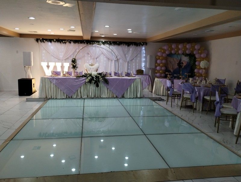 Event hall with illuminated dance floor, decorated tables, and purple accents.