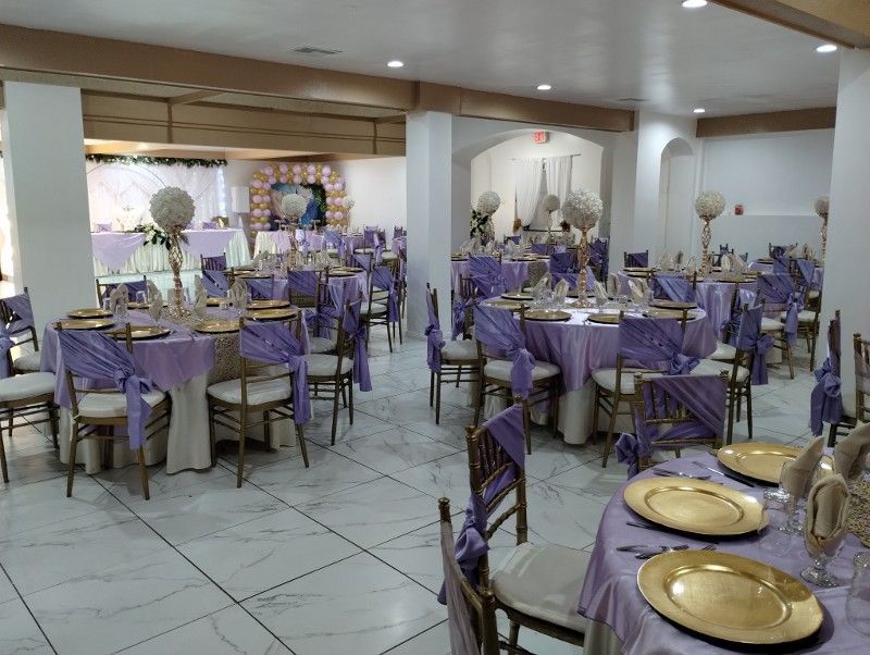Banquet hall with round tables, lilac linens, gold chargers, and floral centerpieces.