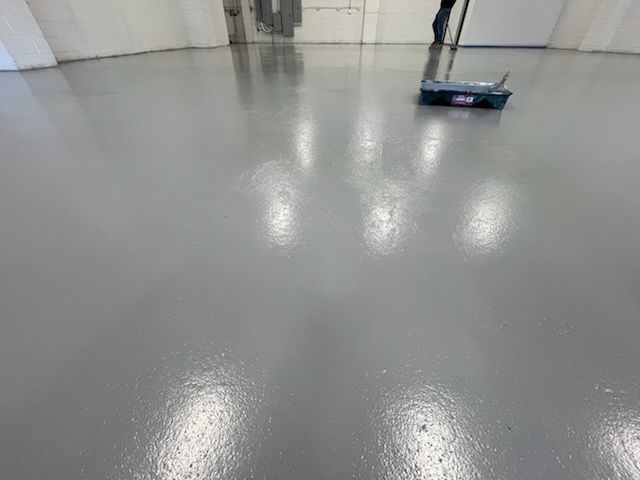 A person is cleaning a concrete floor with a broom.
