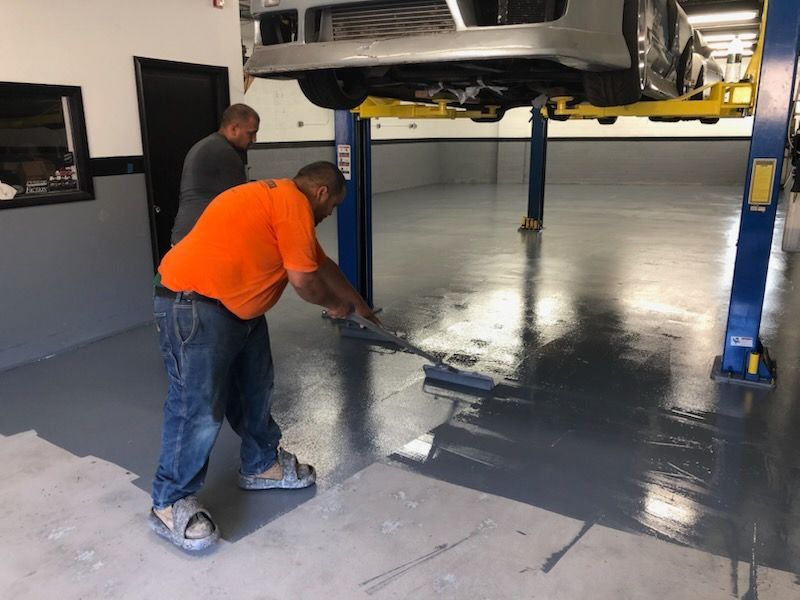 Two men are painting a garage floor in front of a car on a lift.