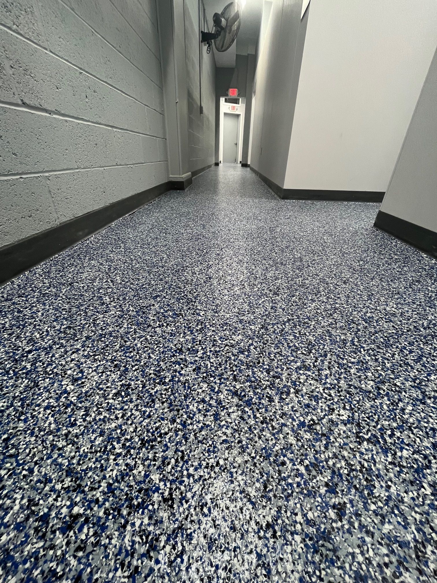 A hallway with a blue and white floor and a fan on the wall.