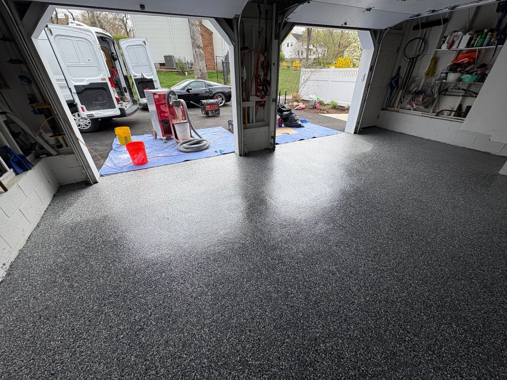 Garage interior with a speckled epoxy floor, open door, and parked vehicles outside.