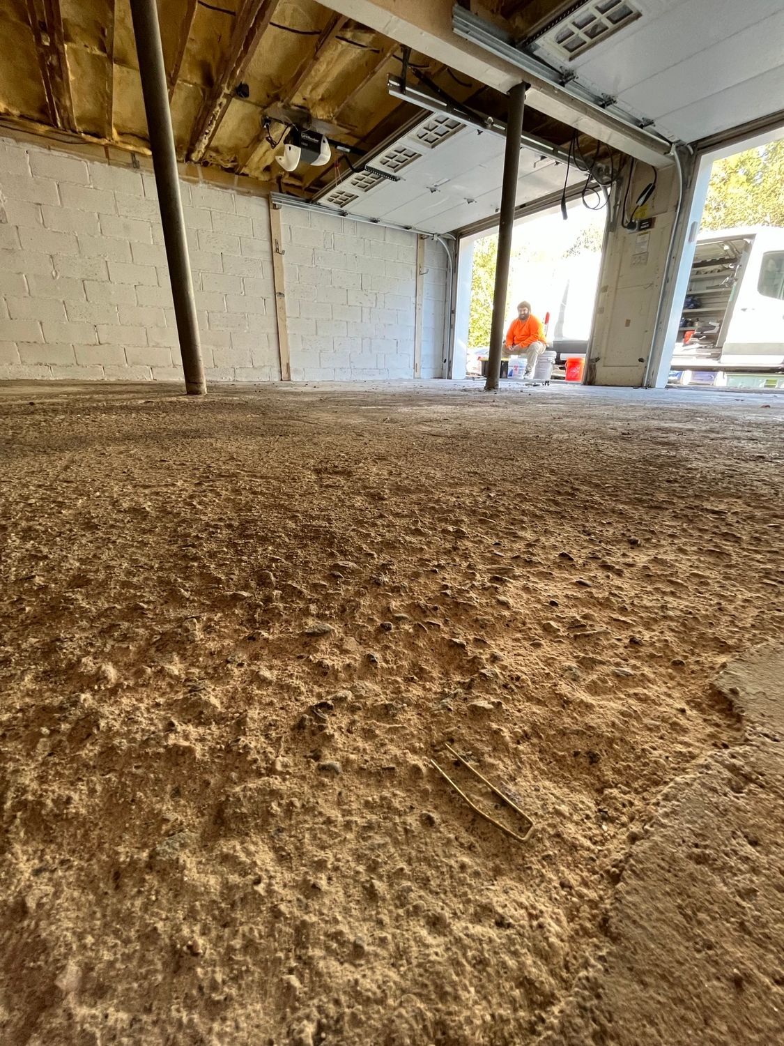 Interior view of a garage under construction with uneven floor and visible support beams. A person is working in the background.