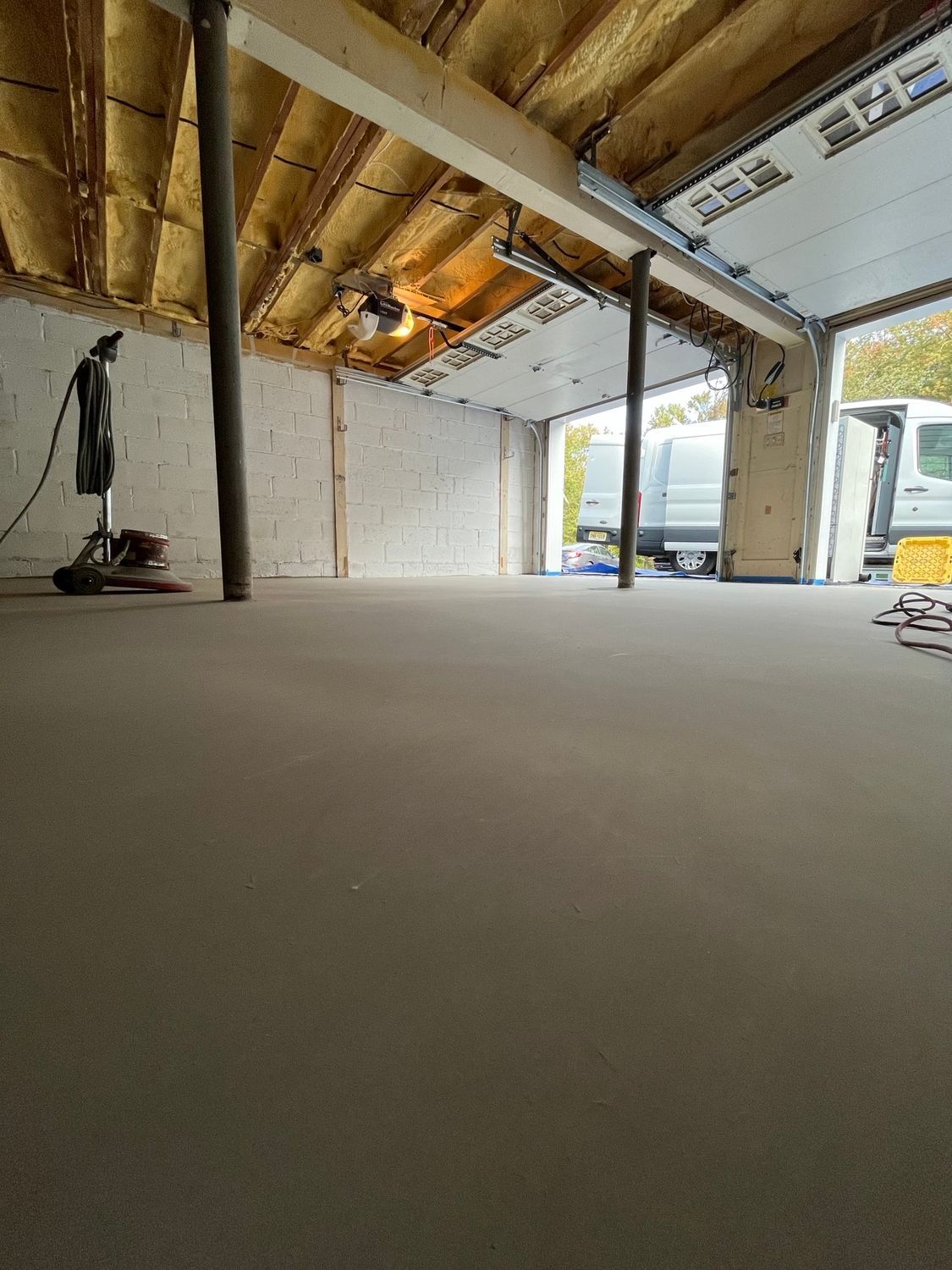 Garage interior, white walls, gray floor, open garage door, two vans outside.