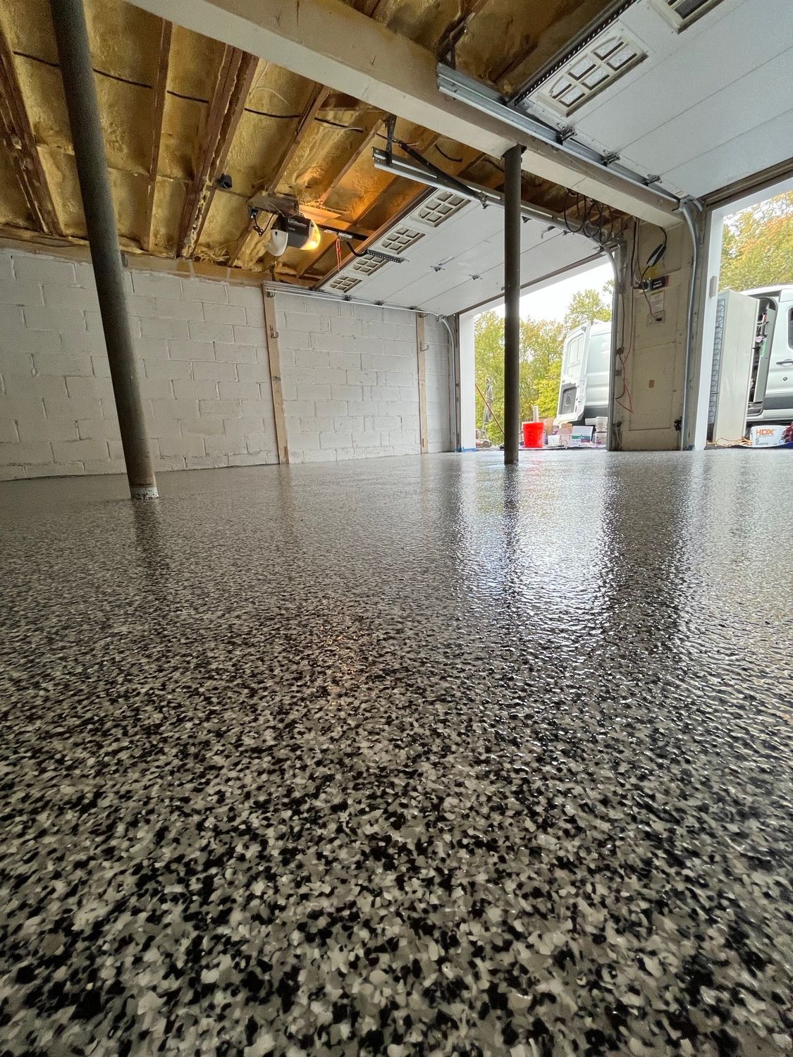 Epoxy garage floor with gray, white, and black flecks, with a partially open garage door and a vehicle visible.