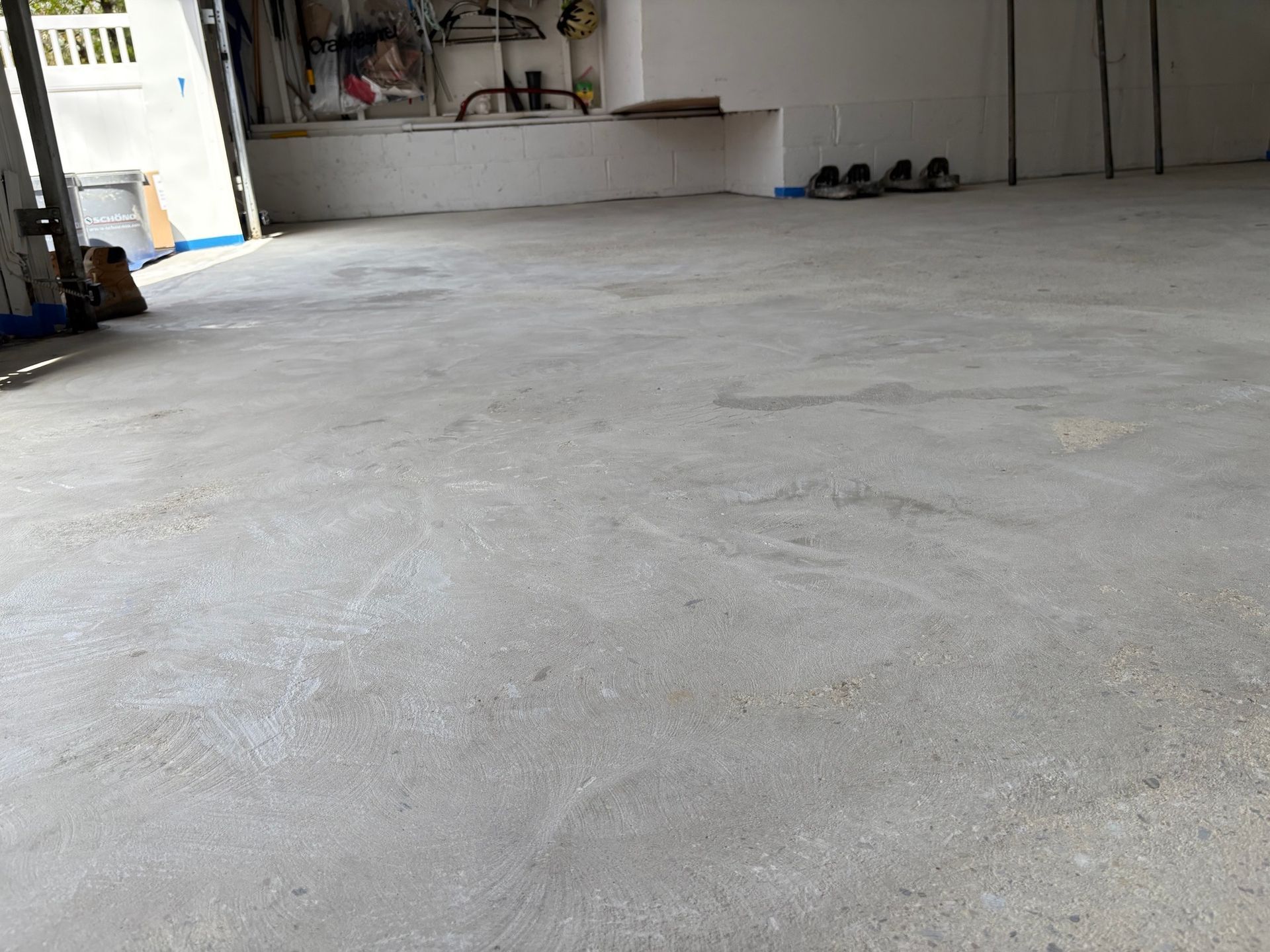 Concrete floor of a garage. The space is mostly empty with some tools and shoes in the background.