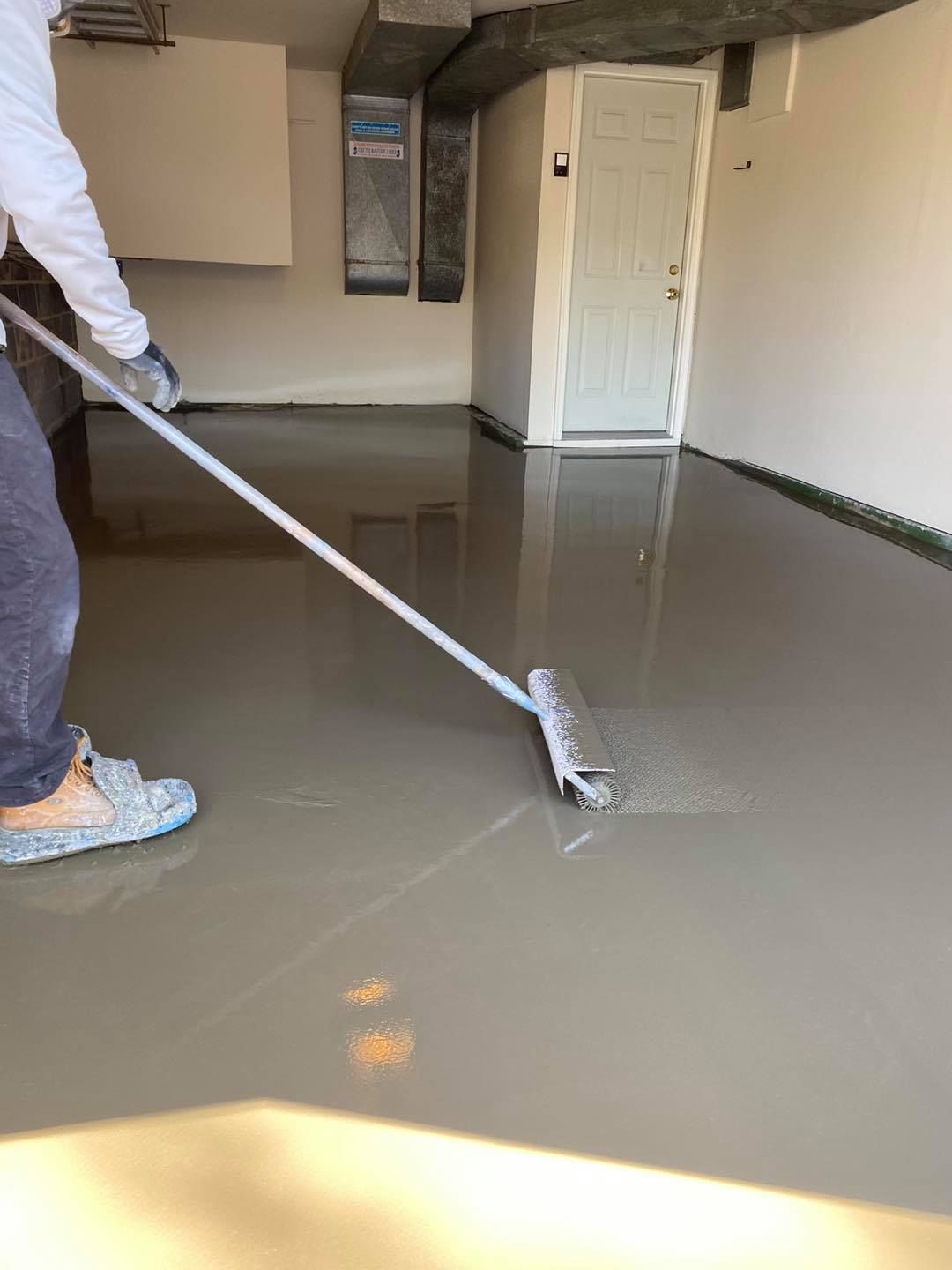 A man is painting a garage floor with a broom.