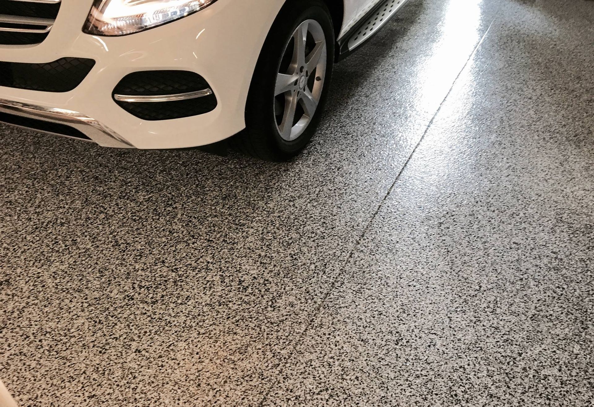 A white car is parked in a garage with a gray floor.