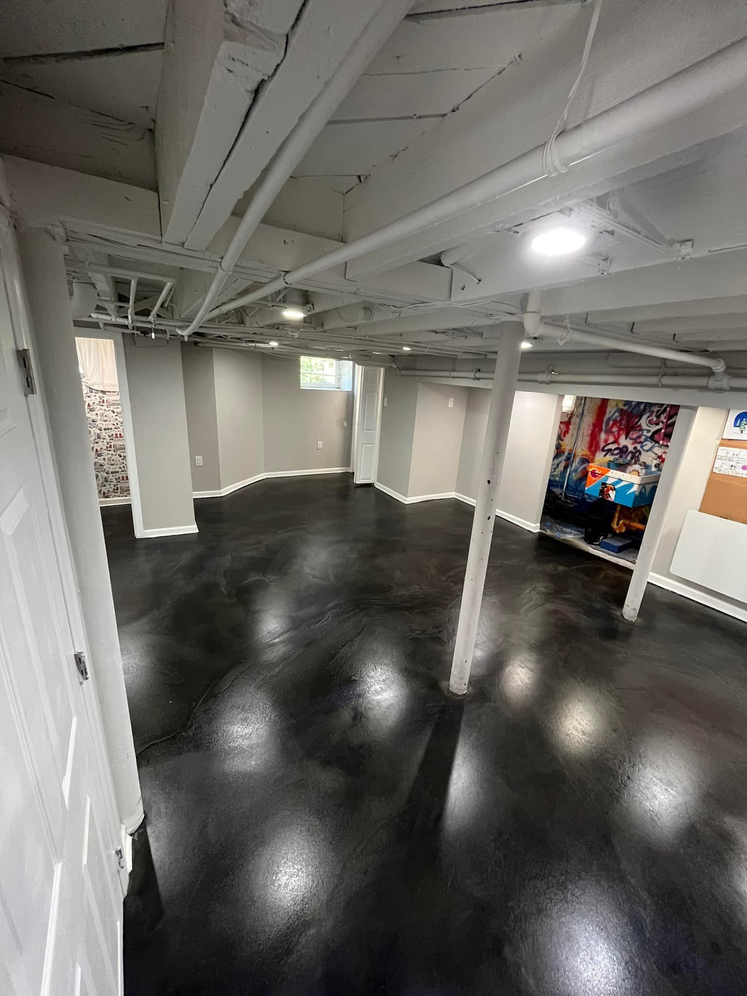 A large empty basement with a black floor and white walls..