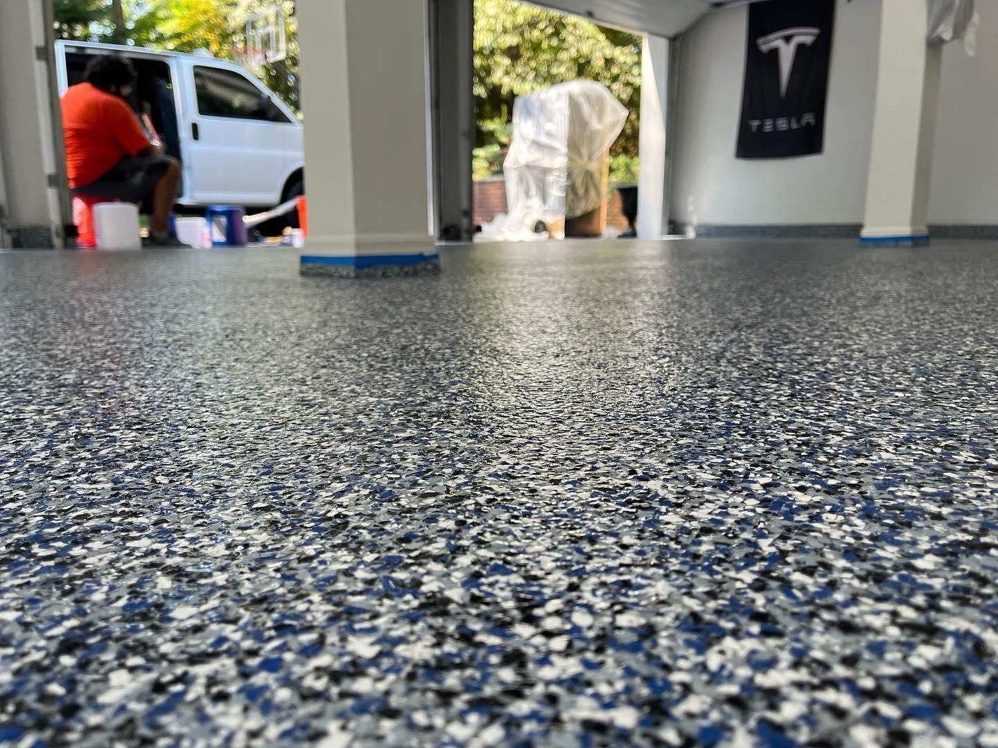 A man is sitting on a bench in a garage with a tesla logo on the wall.