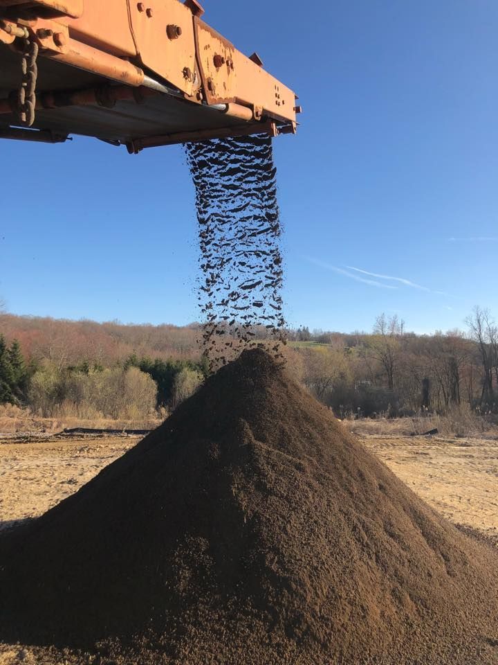 A pile of dirt is being poured from a machine into a pile.